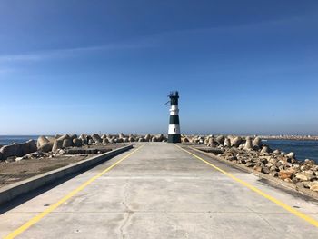 Road leading towards lighthouse by sea against clear sky