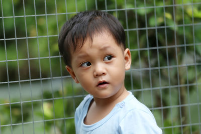 Cute boy looking away against fence outdoors