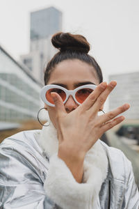 Portrait of woman in sunglasses gesturing against building