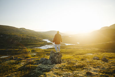 Rear view of woman standing on rock against clear sky