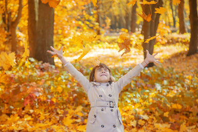 Young woman with arms outstretched standing against yellow flowers