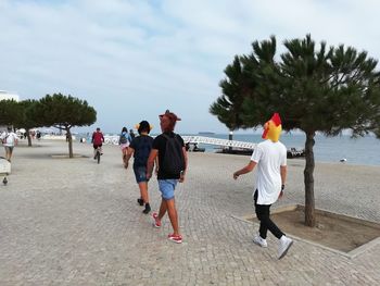 Rear view of people walking on footpath by trees against sky