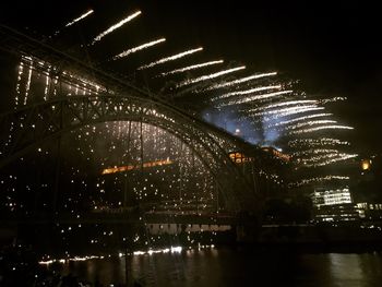 Illuminated city by river against sky at night