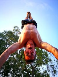 Low angle portrait of man doing handstand against sky