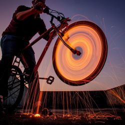 Low angle view of man riding bicycle with wire wool in tire against sky