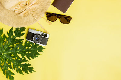 Travel concept with hat, sun glasses, green leaves over the yellow background.