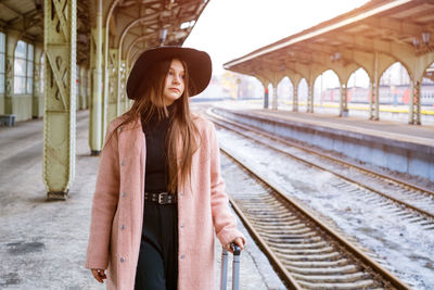 Teenager girl wearing hat looking away standing on railroad station