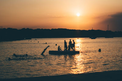 Silhouette people on diving platform in sea during sunset