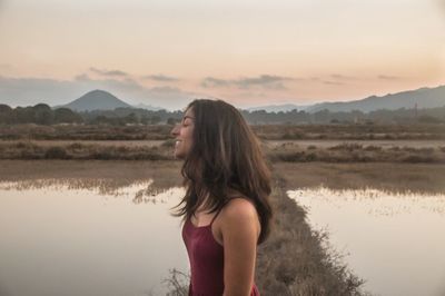 Woman standing by lake against sky during sunset