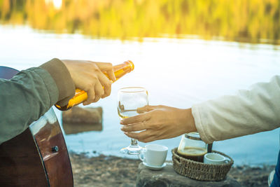 Cropped hand pouring drink for friend by lake