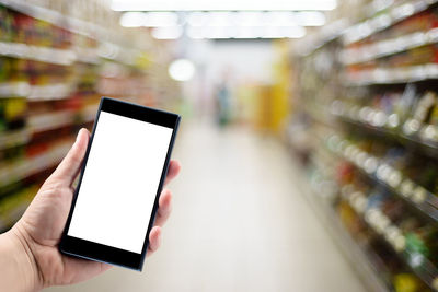 Cropped hand holding mobile phone against supermarket