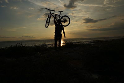 Silhouette boy on beach against sky during sunset