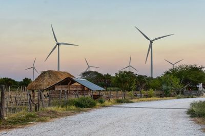 Windmill by road against sky during sunset