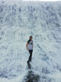 Full length portrait of young woman standing at waterfall