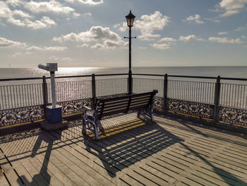 Empty bench on street by sea against sky