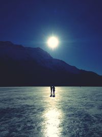 Silhouette person in sea against mountain during sunset