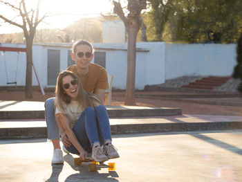 Summer love between a couple of teenagers having a good time on a skate board in the city park