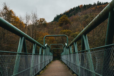 Footbridge leading towards trees against sky