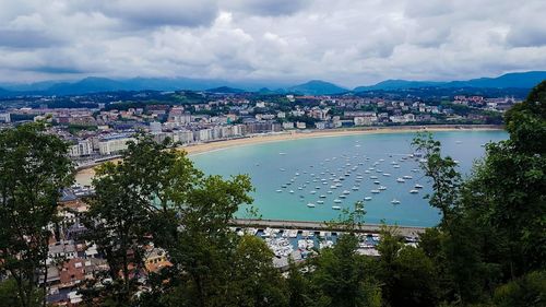 High angle view of boats on sea by city against cloudy sky