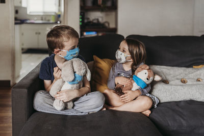 Preschool age girl and school age boy with masks sitting on couch