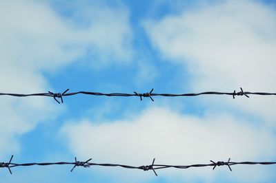 Low angle view of barbed wires against cloudy sky