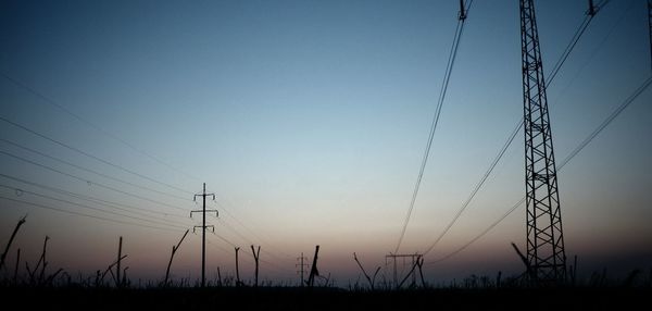 Silhouette electricity pylons on field against clear sky