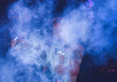 Woman holding cigarette while standing amidst smoke at night