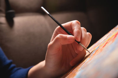 Close-up of a young female artist's hand with a thin brush painting a picture on canvas in a dark