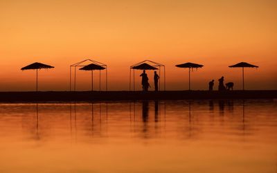 Silhouette people on beach against sky during sunset