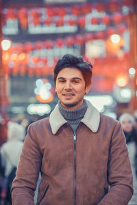 Portrait of smiling man standing against illuminated city at night