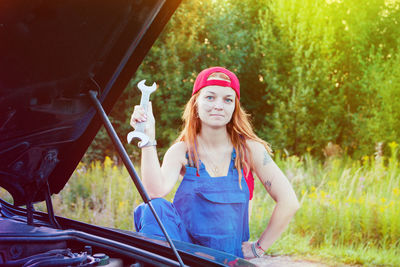 Portrait of confident mechanic repairing breakdown car on road