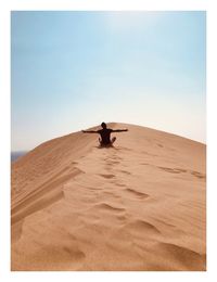 Rear view of man sitting on desert against clear sky