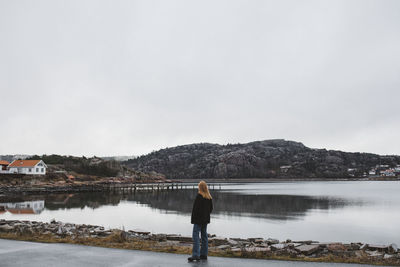 Rear view of man standing by lake against sky