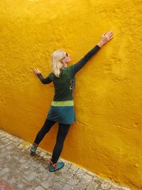 Full length of woman standing against yellow wall