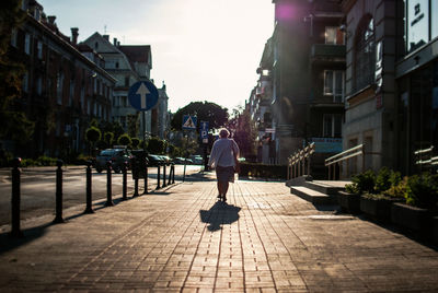 Rear view of woman walking on sidewalk in city during sunny day