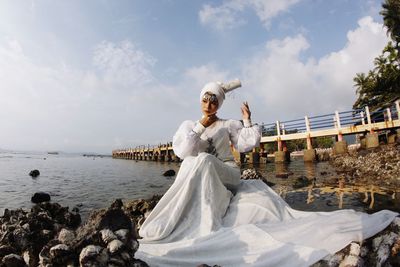 Woman in white dress sitting on rock by sea