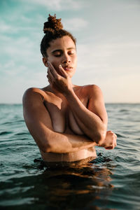 Shirtless young woman swimming in sea against sky