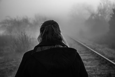 Rear view of woman on railroad tracks against sky