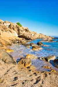 Rocks in sea against clear blue sky