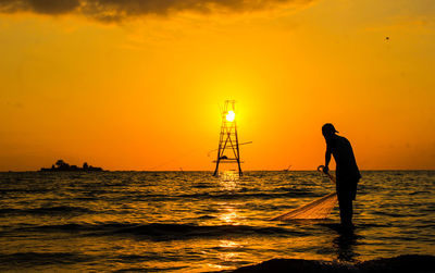 Silhouette man standing on sea against orange sky