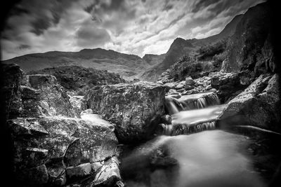 Scenic view of waterfall amidst mountains against sky