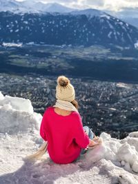 Rear view of woman sitting snowcapped mountain