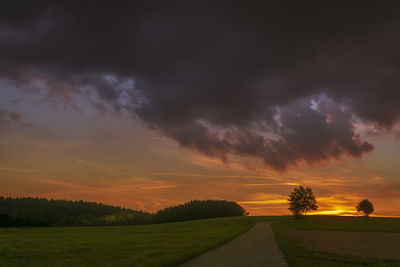 Scenic view of road amidst field against sky during sunset