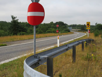 Road sign by trees on field against sky