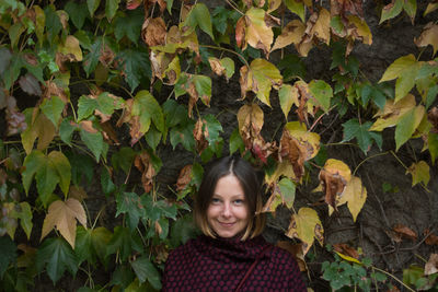 Portrait of smiling woman standing against leaves