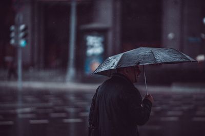 Rear view of man holding umbrella in rainy season