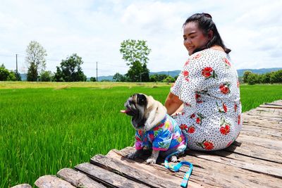 Smiling woman with dog sitting on boardwalk by agricultural field