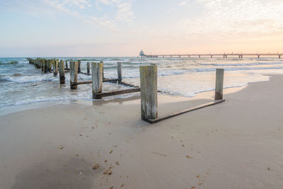 Wooden posts on beach against sky during sunset