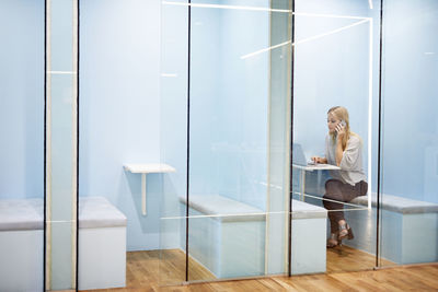 Serious businesswoman talking on mobile phone while using laptop in cubicle at office