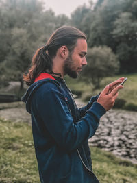 Side view of young man using mobile phone while standing in park
